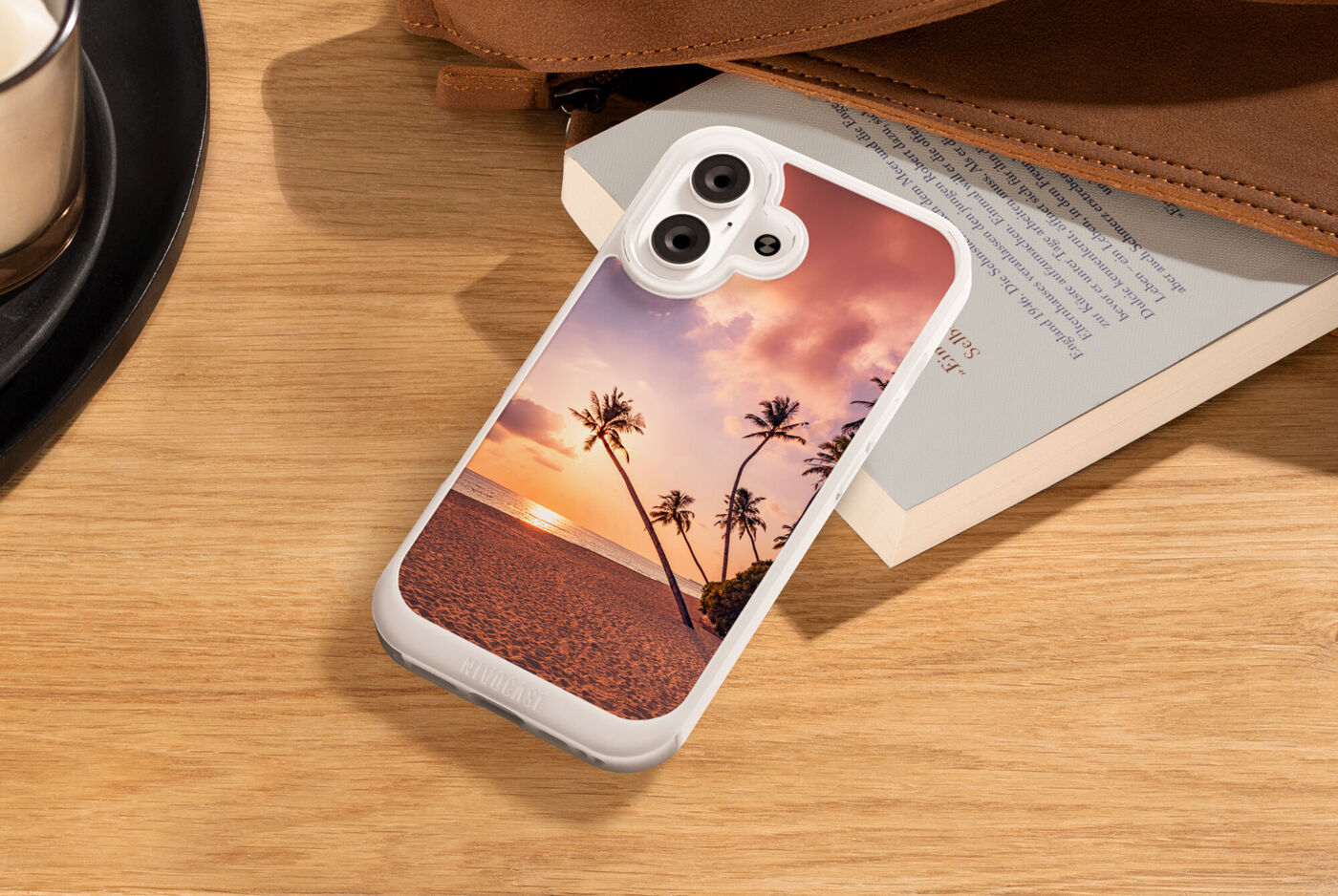 Smartphone mit Hülle, die ein Strandmotiv mit Palmen und Sonnenuntergang zeigt, liegt auf einem Holztisch.